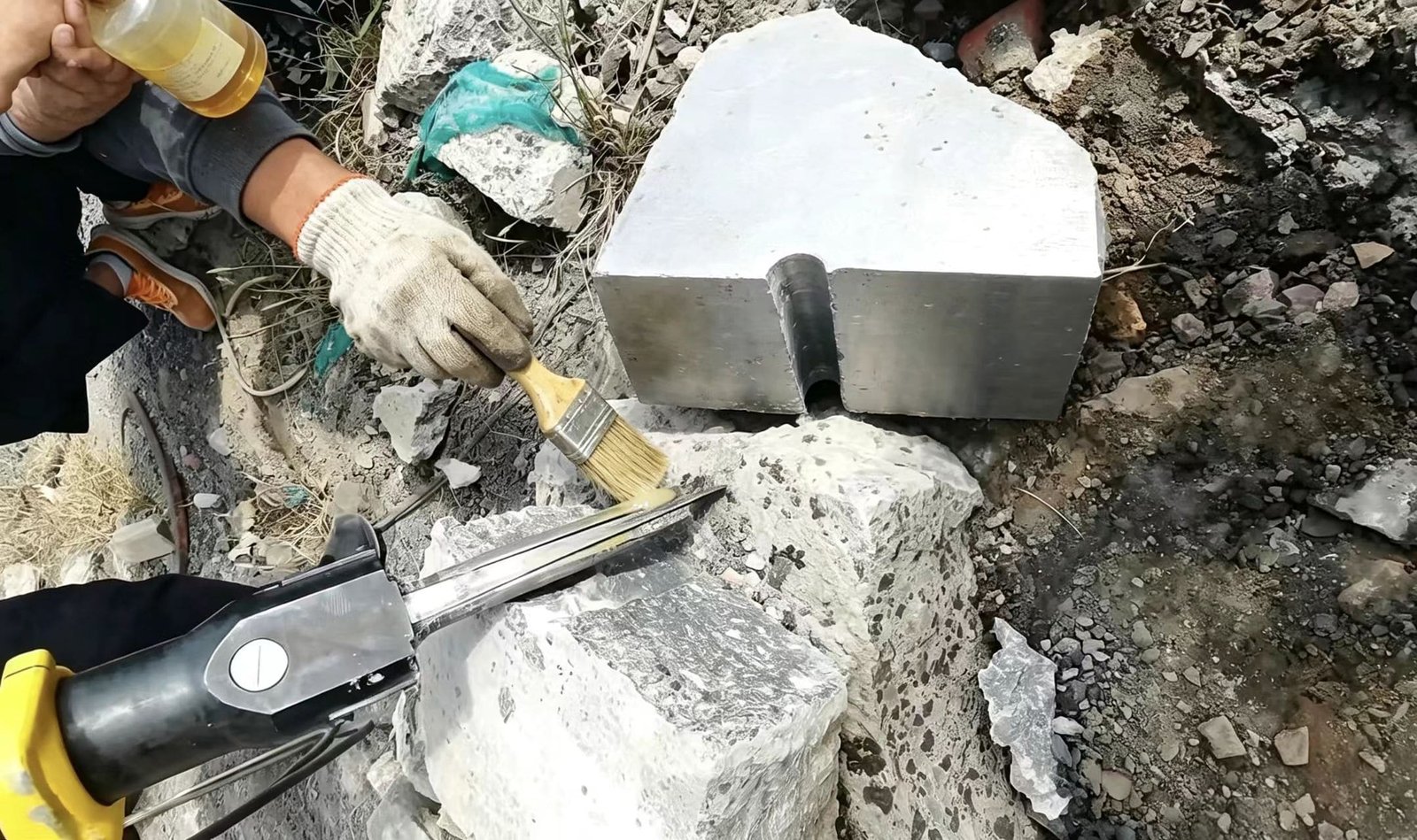 Technician applying lubricant to the wedge set of a hydraulic splitter, a key best practice for the rock splitting method.